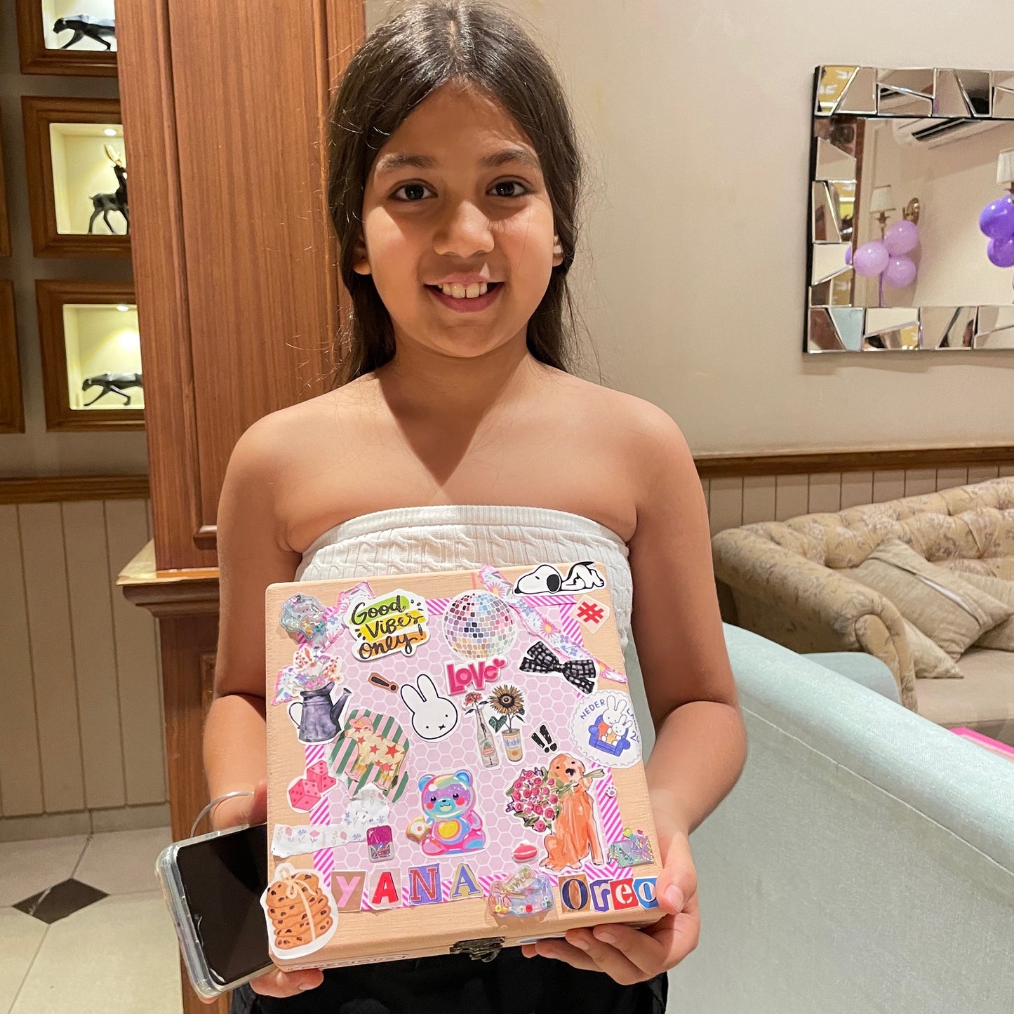 Young girl holding a decorated book with stickers at a party.