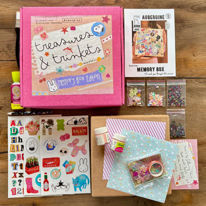 Collection of stationery items including a pink box labeled 'treasures & trinkets' on a wooden surface.