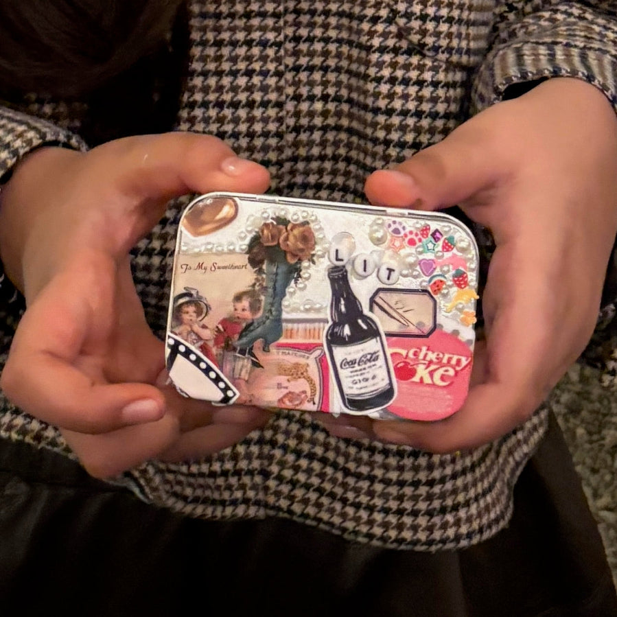 Small decorative tin held by hands with vintage-style graphics on a checkered fabric background.