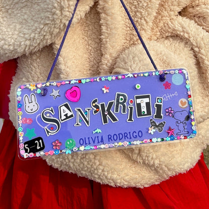 Decorative nameplate with colorful designs and text, hanging on a textured surface.