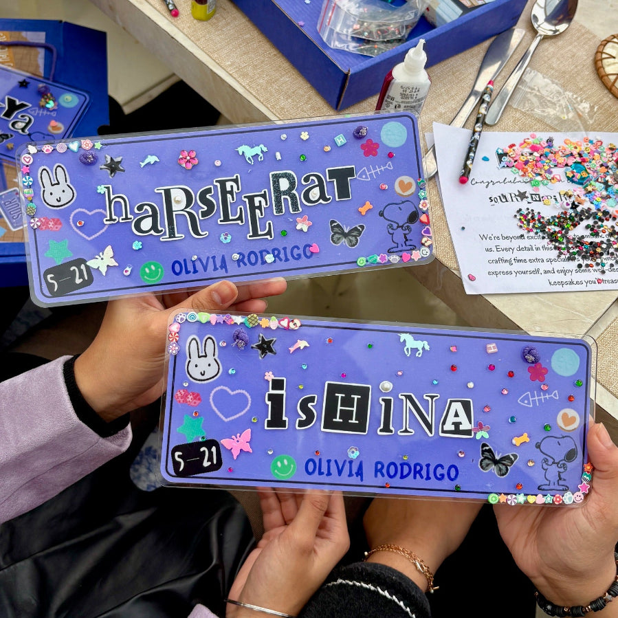 Two personalized doorplates held by hands on a table with various items.
