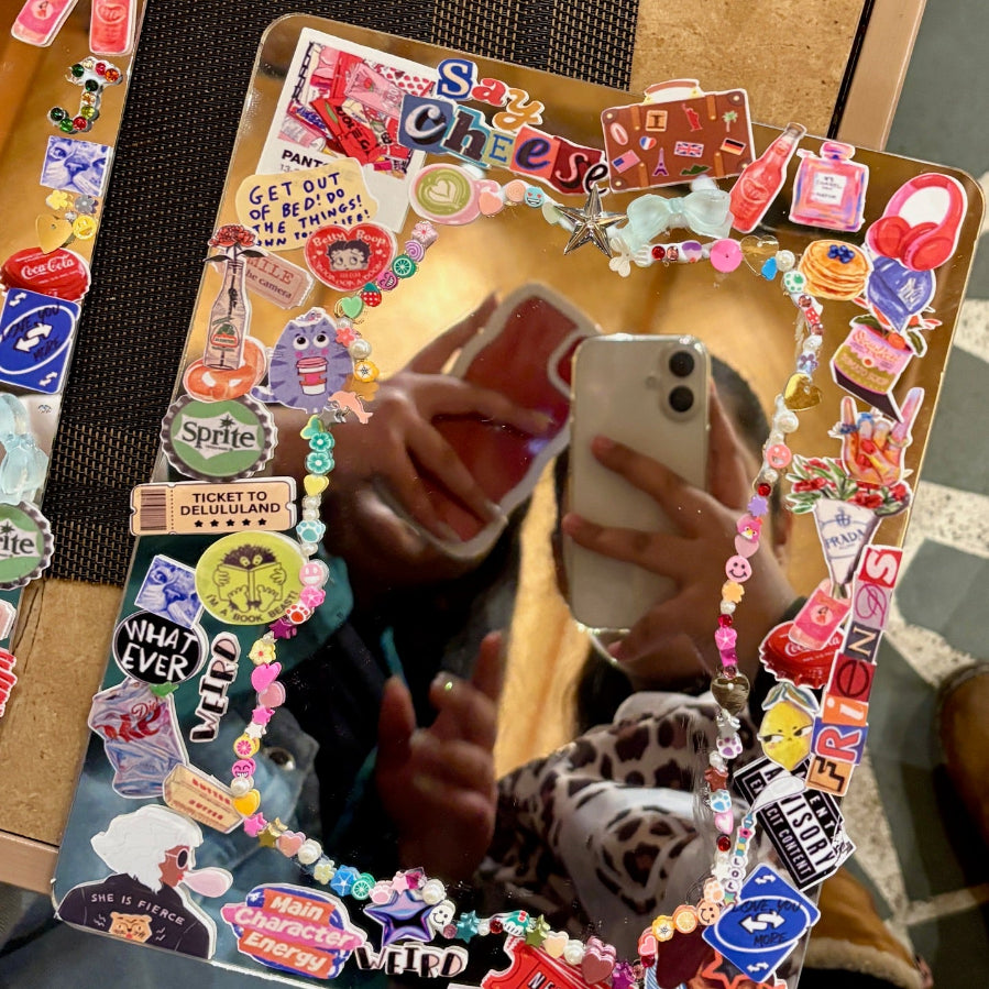 Decorative mirror with colorful stickers and text, held by a person.