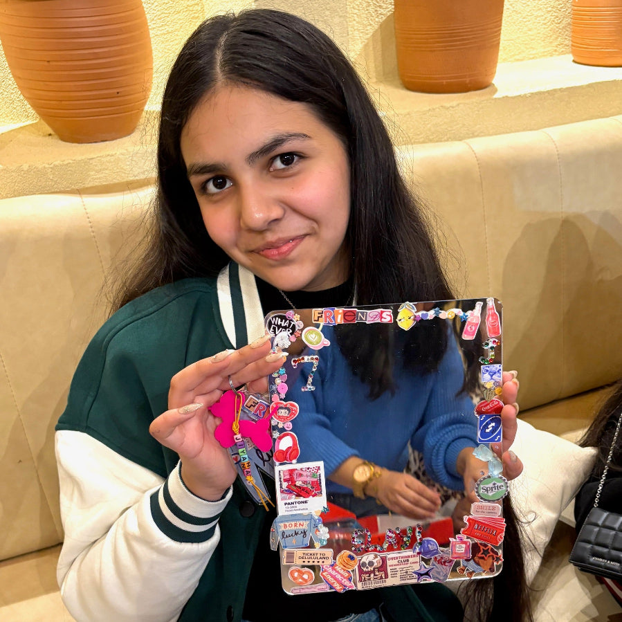 Person holding a crafted mirror with various stickers in a casual indoor setting.